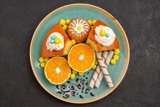 Top view delicious cake slices with pipe cookies and sliced tangerines on dark background fruit citrus cake pie cookie sweet tea