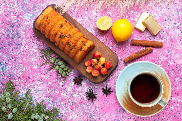 Top view delicious cake sweet and yummy with sweet cherries cinnamon and cup of tea on pink desk.