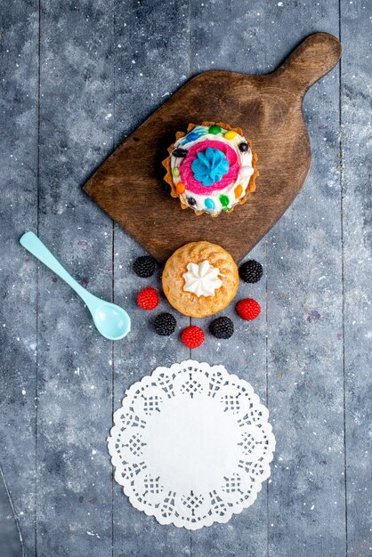 top view of delicious cake with cream and candies along with berries cookie cakes on light desk, cake biscuit sweet bake candy