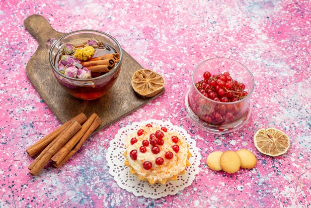 Вид сверху восхитительный торт со сливками и красной клюквой вместе с корицей и чашкой чая на ярком письменном торте