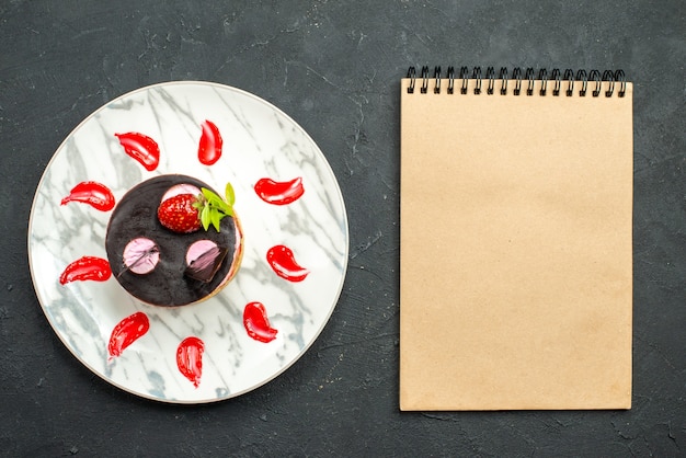 Free photo top view delicious cake with strawberry and chocolate on oval plate a notebook on dark background