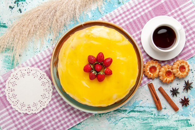 Top view delicious cake with yellow syrup fresh red strawberries and cup of tea on the blue desk biscuit cake bake sweet sugar pie tea