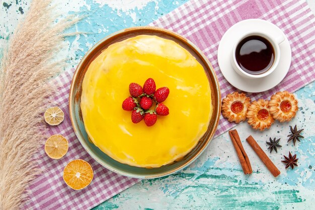 Top view delicious cake with yellow syrup fresh red strawberries and cup of tea on blue surface biscuit cake bake sweet sugar pie tea