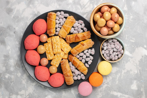 Вид сверху вкусные торты с рогаликами, крекеры, конфеты на светло-белом столе, бисквитное печенье, сладкий сахарный пирог
