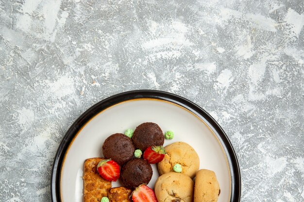 Вид сверху вкусные торты с печеньем и клубникой на белом столе бисквитный сахарный торт сладкий пирог чайное печенье