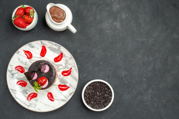 Top view delicious cheesecake with strawberry and chocolate on oval plate bowl of strawberries and chocolate on dark isolated background