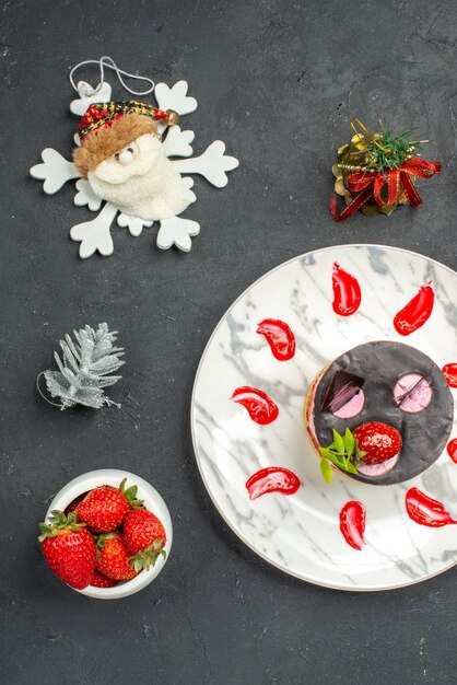 Top view delicious cheesecake with strawberry and chocolate on oval plate bowl of strawberries xmas toys on dark background