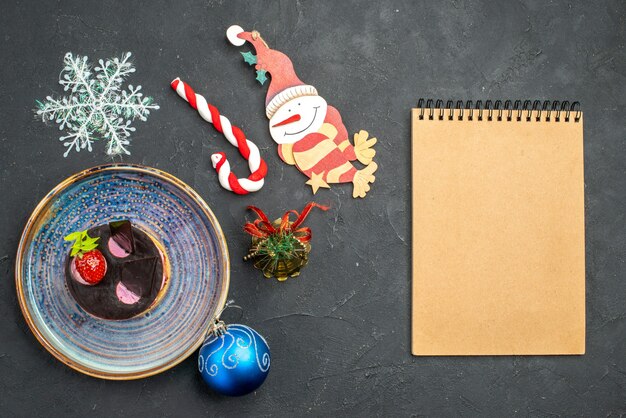 Вид сверху вкусного чизкейка с клубникой и шоколадом на тарелке, рождественские детали записной книжки на темном изолированном фоне