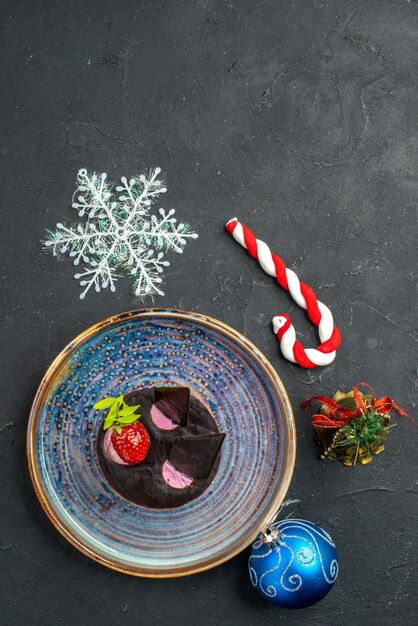 Вид сверху вкусный чизкейк с клубникой и шоколадом на тарелке рождественских игрушек на темном изолированном фоне