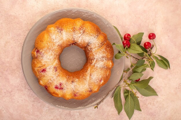 A top view delicious cherry cake round formed inside grey plate on the pink desk cake biscuit sugar sweet