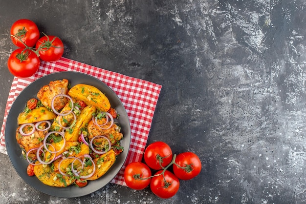 Top view of delicious chicken meal with potatoes and vegetables greens on folded red stripped towel tomatoes with stems on dark color background with free space