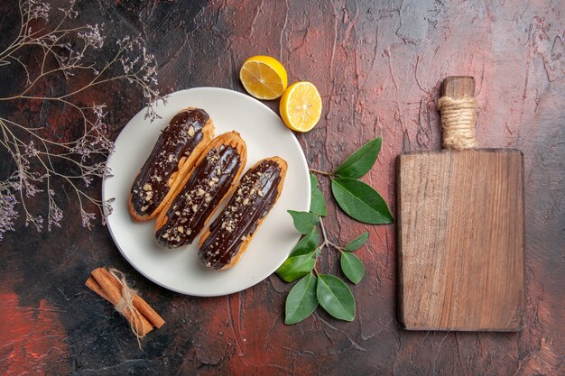 Top view delicious choco eclairs inside plate on dark table cake pie sweet dessert