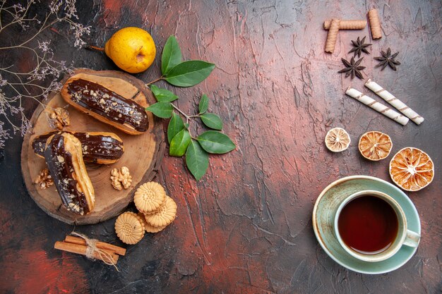 Top view delicious choco eclairs with cup of tea on a dark table dessert sweet cake