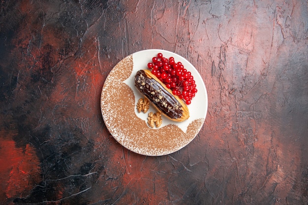 Вид сверху вкусные шоколадные эклеры с красными ягодами на темном столе, пирог, десерт, торт, сладкий