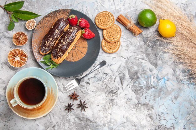 Вид сверху вкусные шоколадные эклеры с чаем на белом столе, десертное печенье