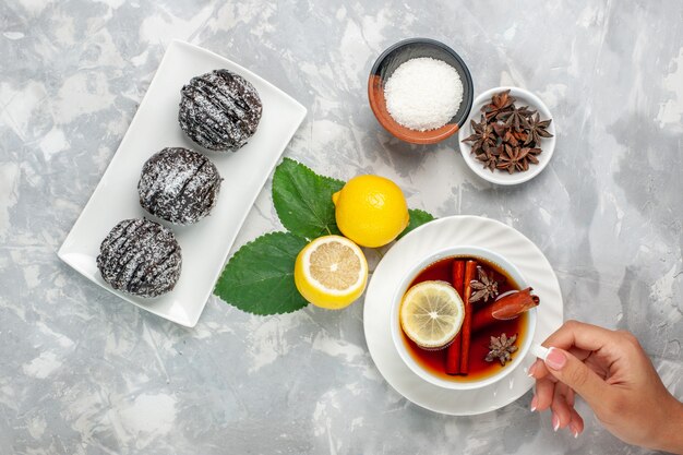 Вид сверху вкусные шоколадные пирожные, маленькие круглые, с лимоном и чашкой чая на белой поверхности, фруктовый торт, бисквит, сладкое сахарное печенье