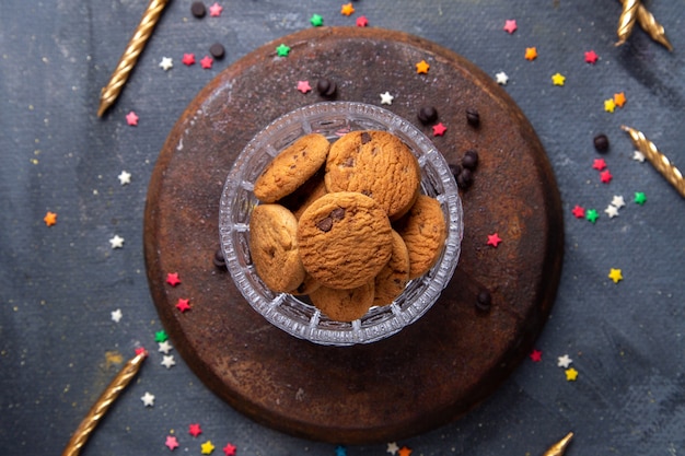 Top view delicious chocolate cookies inside transparent bowl with candles on the dark-grey background cookie biscuit sugar tea sweet