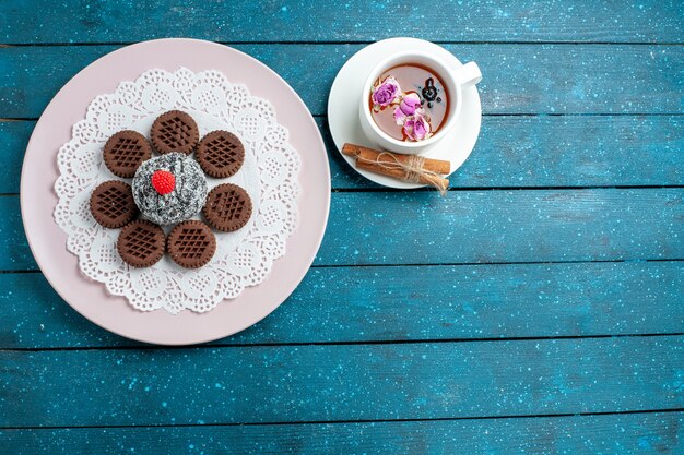 Top view delicious chocolate cookies with cup of tea on blue rustic desk biscuit tea cookie sweet cake sugar