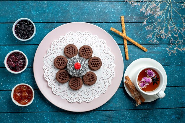 Top view delicious chocolate cookies with jam and cup of tea on a blue rustic desk biscuit tea cookie sweet cake sugar