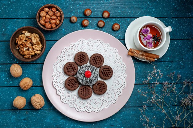 Top view delicious chocolate cookies with nuts and cup of tea on blue rustic desk biscuit tea cookie sweet cake sugar