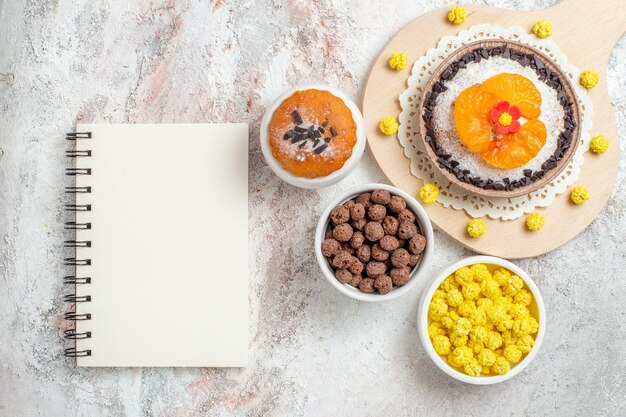 Top view delicious chocolate dessert with tangerines and candies on a white background cream dessert biscuit cake fruit