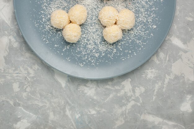 Вид сверху вкусных кокосовых конфет внутри синей тарелки на белом столе