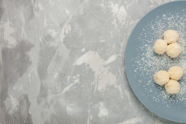 Top view of delicious coconut candies inside blue plate on white desk