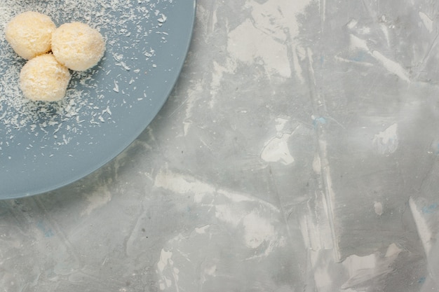 Top view of delicious coconut candies inside blue plate on white surface