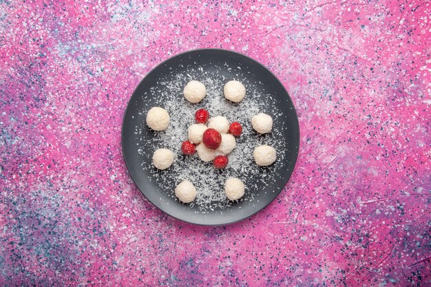 Top view of delicious coconut candies sweet balls on light pink surface