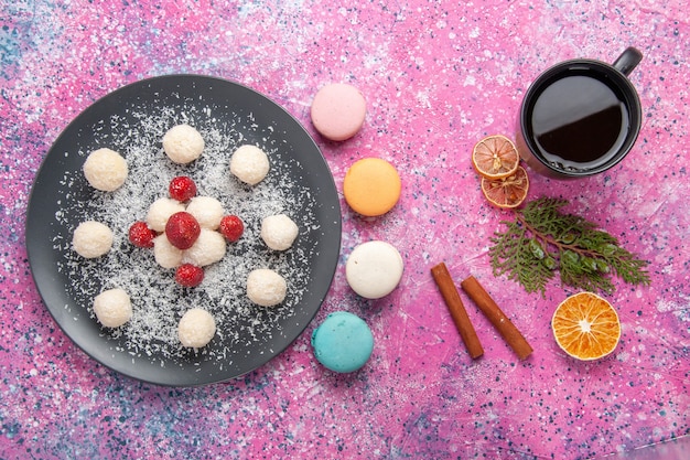 Top view of delicious coconut candies sweet balls with french macarons on pink surface