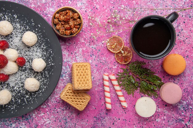 Top view of delicious coconut candies sweet balls with french macarons on the pink surface