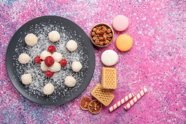 Top view of delicious coconut candies sweet balls with french macarons and waffles on pink surface