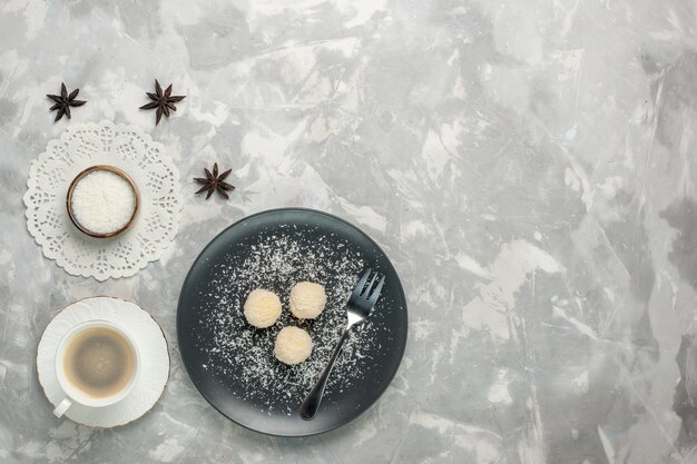 Top view of delicious coconut candies with coffee on white desk