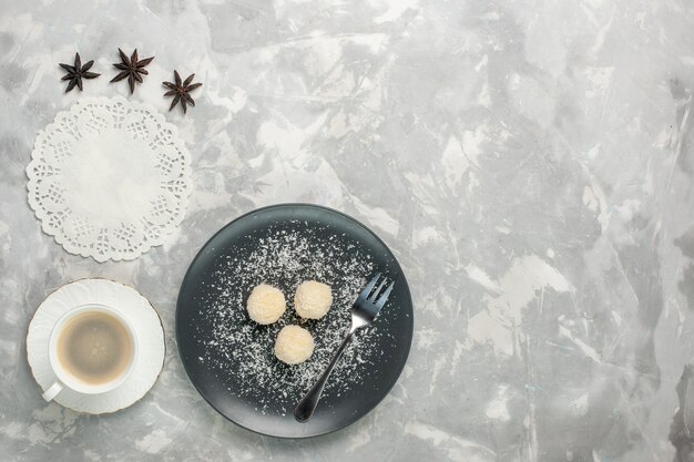 Top view of delicious coconut candies with coffee on white surface