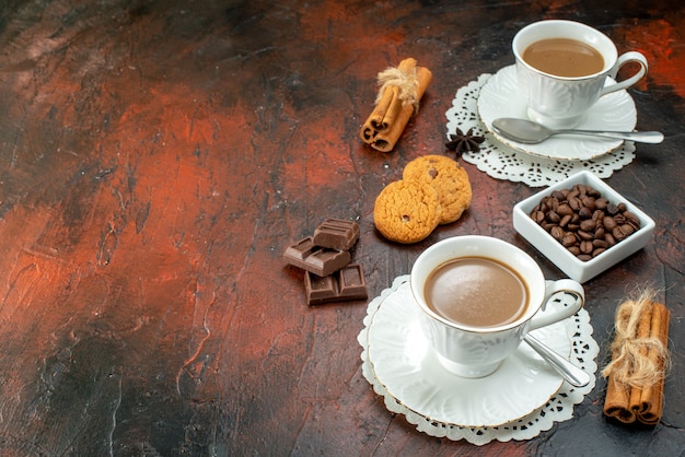 Top view of delicious coffee in white cups on napkins cookies cinnamon limes chocolate bars on the left side on mixed color background