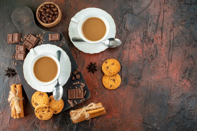 Top view of delicious coffee in white cups on wooden cutting board cookies cinnamon limes chocolate bars