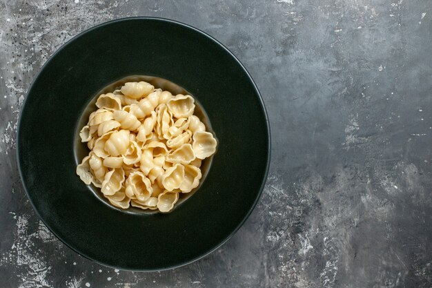 Top view of delicious conchiglie on a black plate on gray background