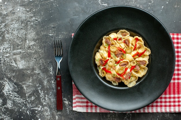 Top view of delicious conchiglie with vegetables and greens on a plate and knife on red stripped towel on gray background