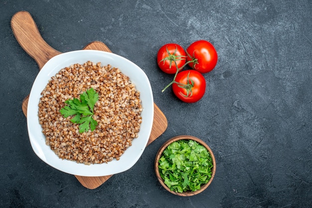 Вид сверху вкусной приготовленной гречки со свежими помидорами и зеленью на сером пространстве