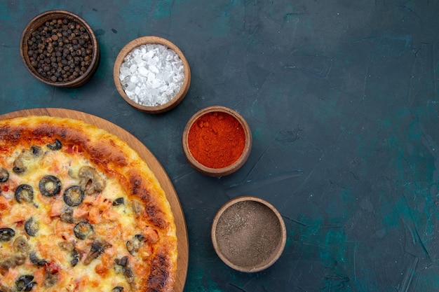 Top view of delicious cooked pizza with different seasonings on the dark blue desk