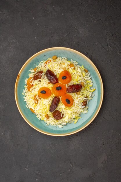 Top view of delicious cooked plov rice with different raisins inside plate on dark grey surface