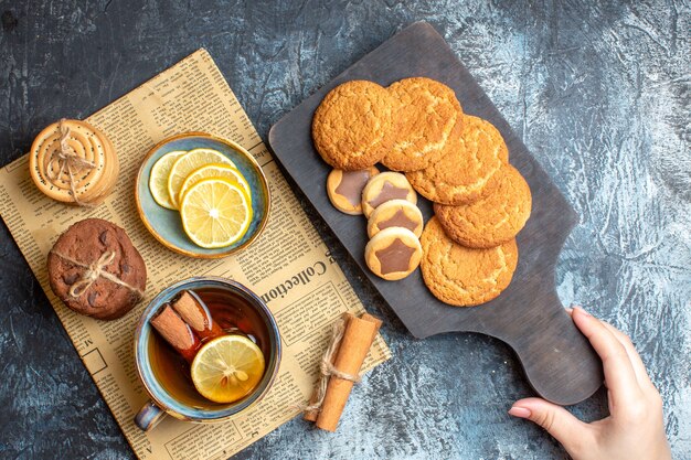 Free photo top view of delicious cookies and a cup of black tea with cinnamon lemon on an old newspaper