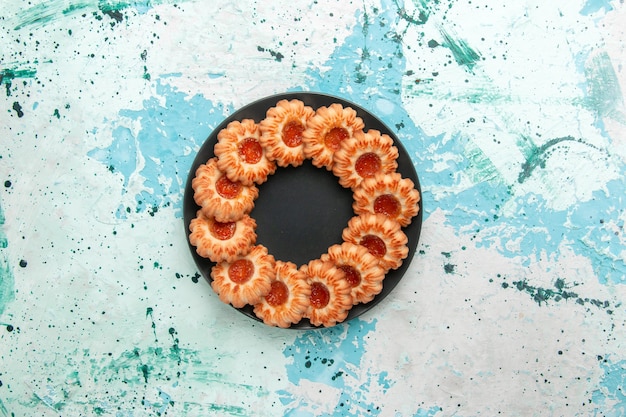 Top view delicious cookies round formed with jam inside black plate on light-blue background cookie sugar sweet biscuit cake