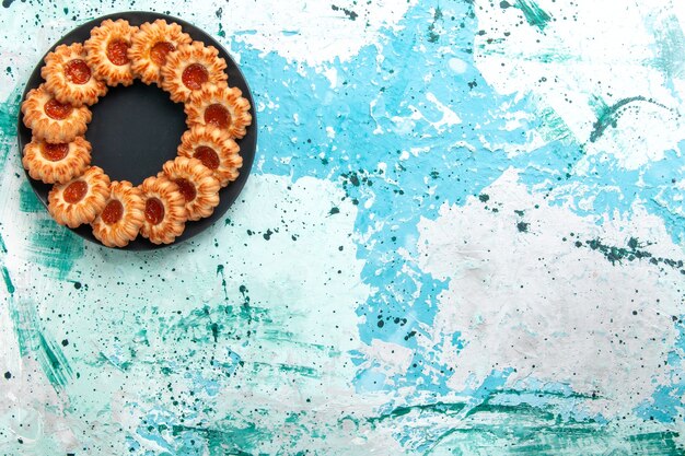 Вид сверху вкусного печенья круглой формы с джемом внутри черной тарелки на голубом фоне печенье сахарный сладкий бисквитный торт