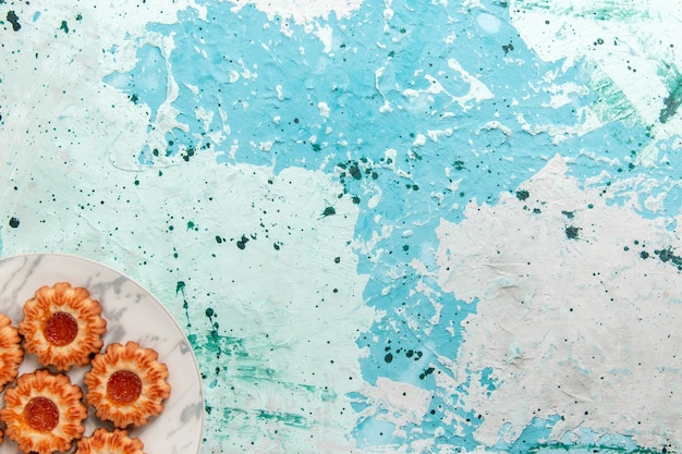 Вид сверху вкусного печенья круглой формы с джемом внутри тарелки на голубом фоне печенье сахарный сладкий бисквитный торт
