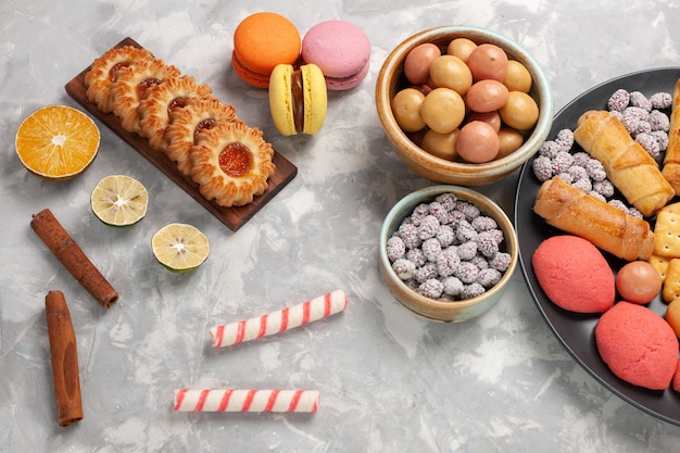 Top view delicious cookies with cinnamon macarons and candies on white desk cookie biscuit sugar sweet cake