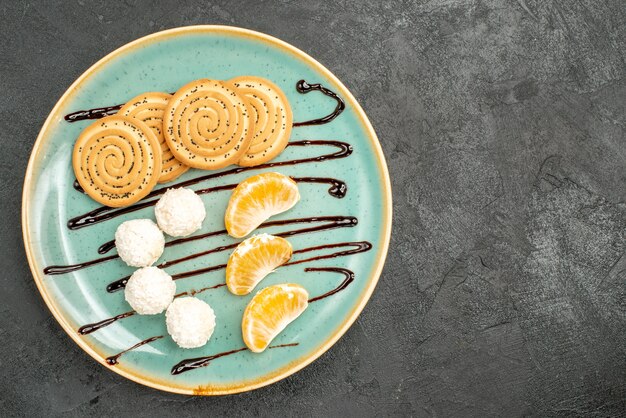 Top view delicious cookies with coconut candies and fruits on the grey desk