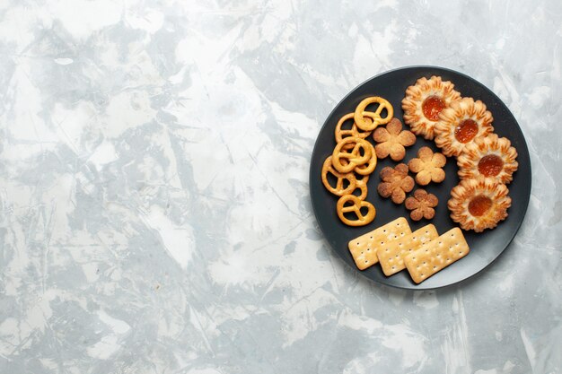 Top view delicious cookies with crackers and crisps inside plate on light white desk cookie biscuit sugar sweet tea crisp