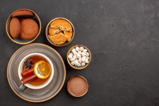 Top view delicious cookies with cup of tea on dark surface sugar cookie dessert biscuit sweet