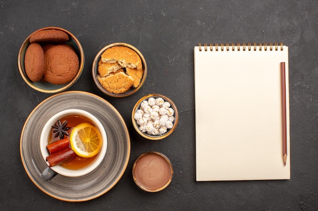 Top view delicious cookies with cup of tea on dark surface sugar cookies dessert biscuit sweet